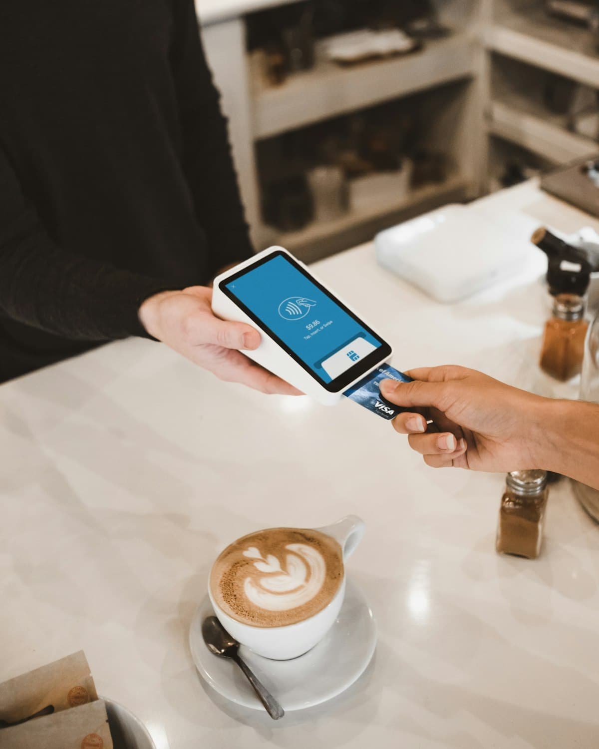 A customer paying by card at a café counter, a latte beside the terminal
