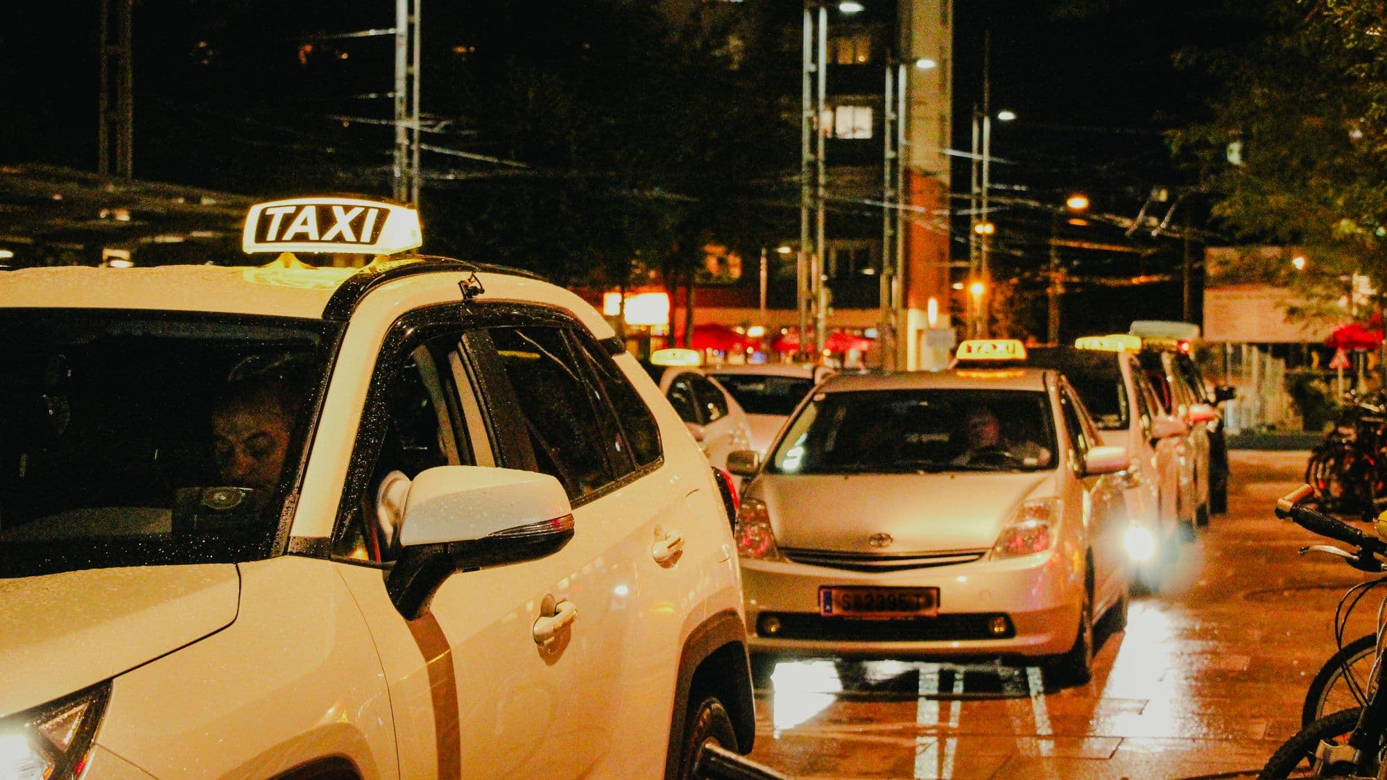A rank of taxis waiting under street lights at night