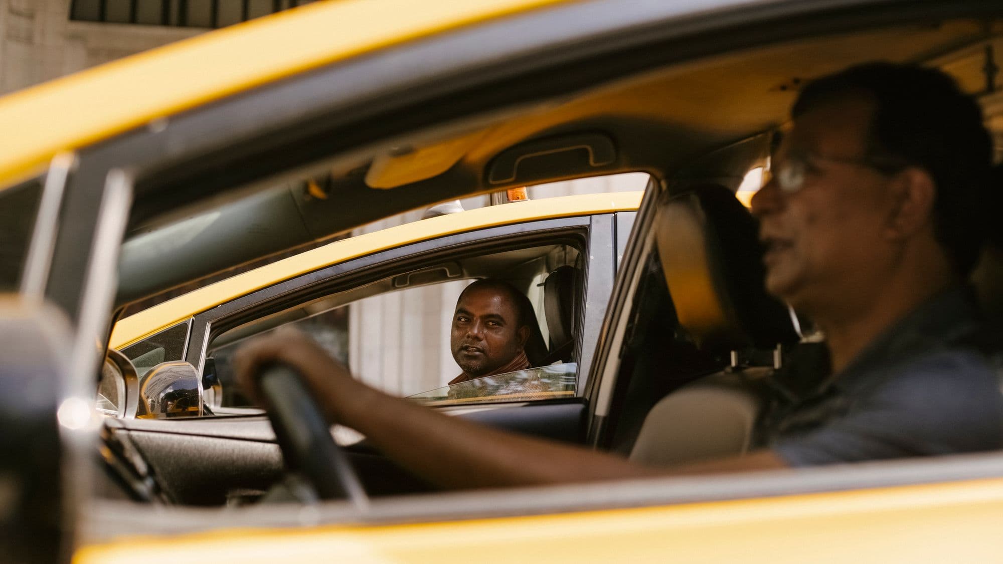 Two drivers talking through open windows between their cars in daylight