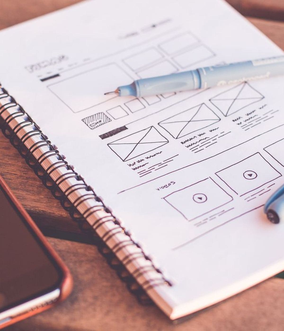 A hand-drawn page layout sketched in a notebook on a wooden desk