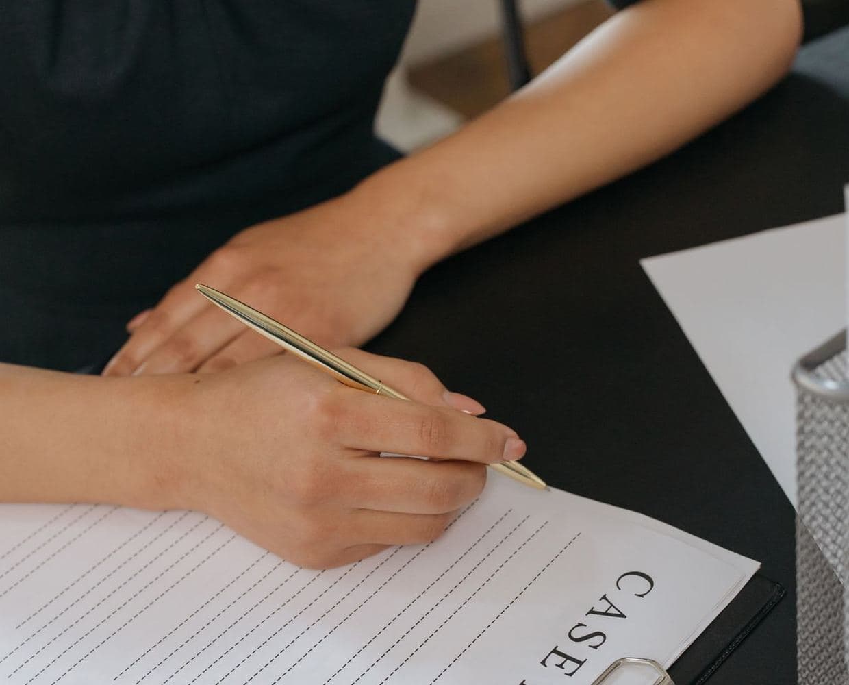 A hand filling in a paper form beside a laptop