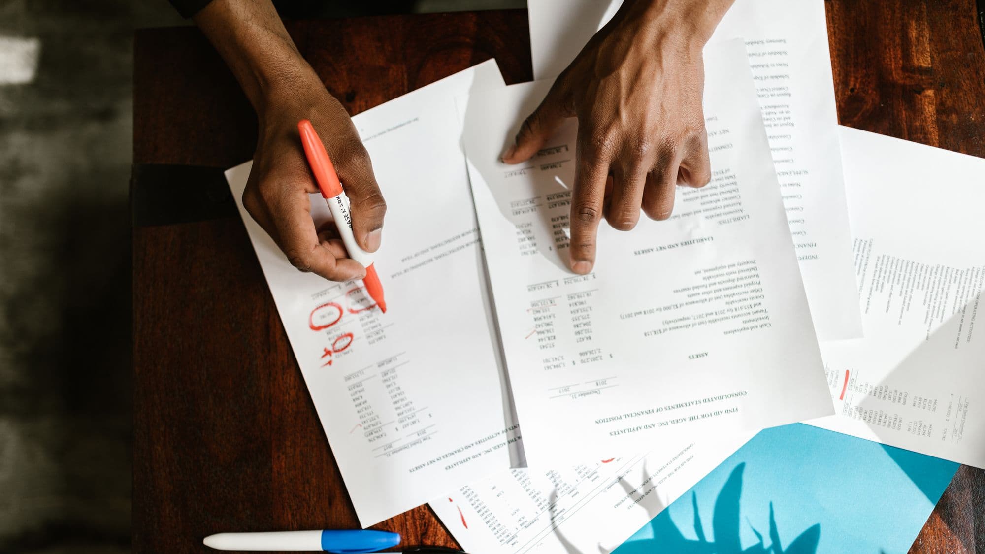 Hands marking up financial documents on a desk