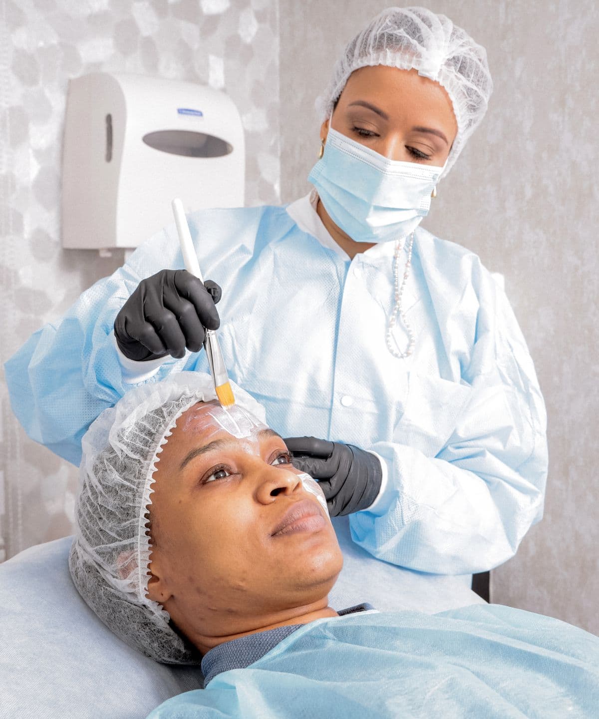 A practitioner carrying out a facial treatment on a patient in a clinic room
