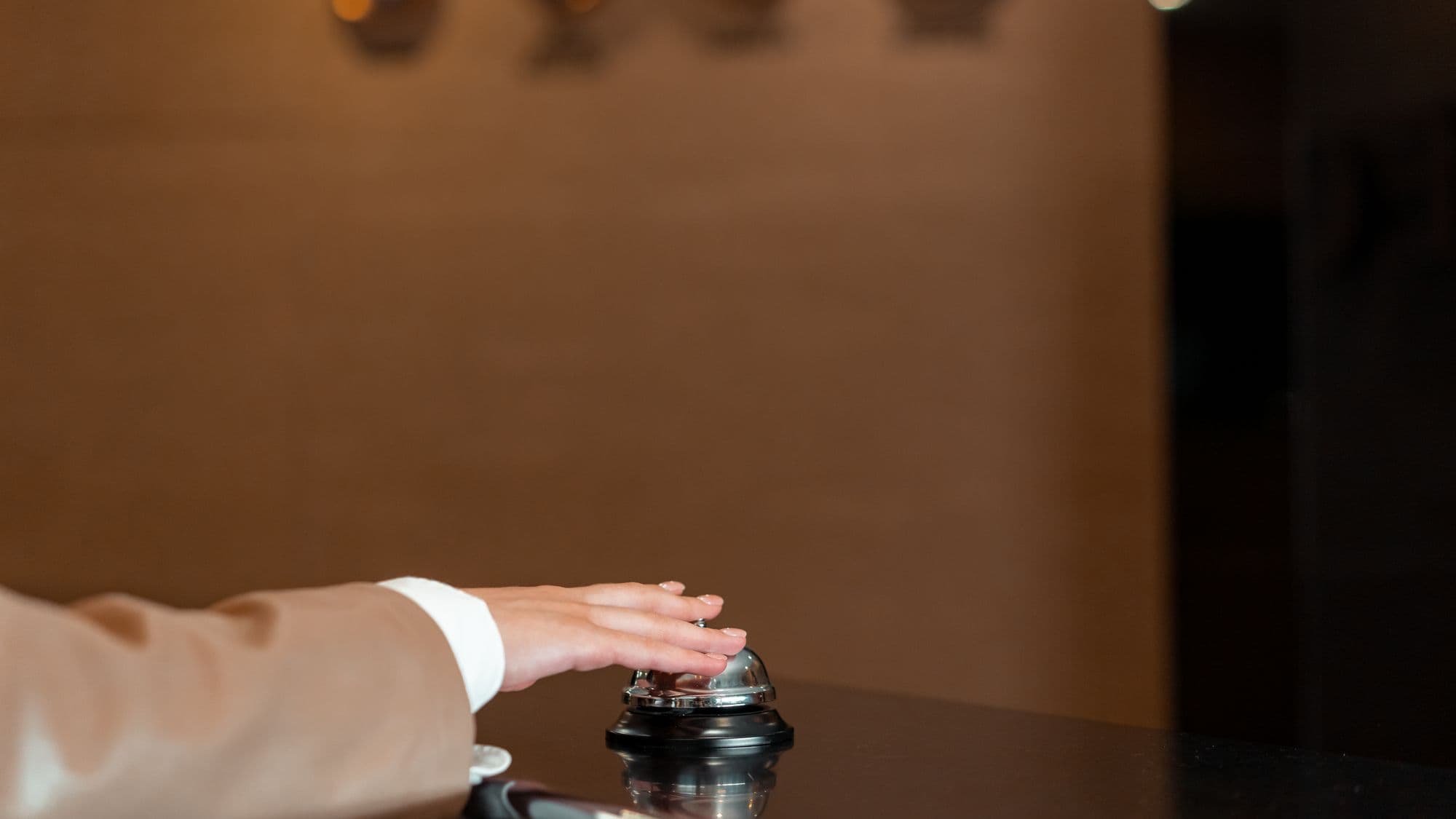 A hand resting on a service bell at a hotel reception desk