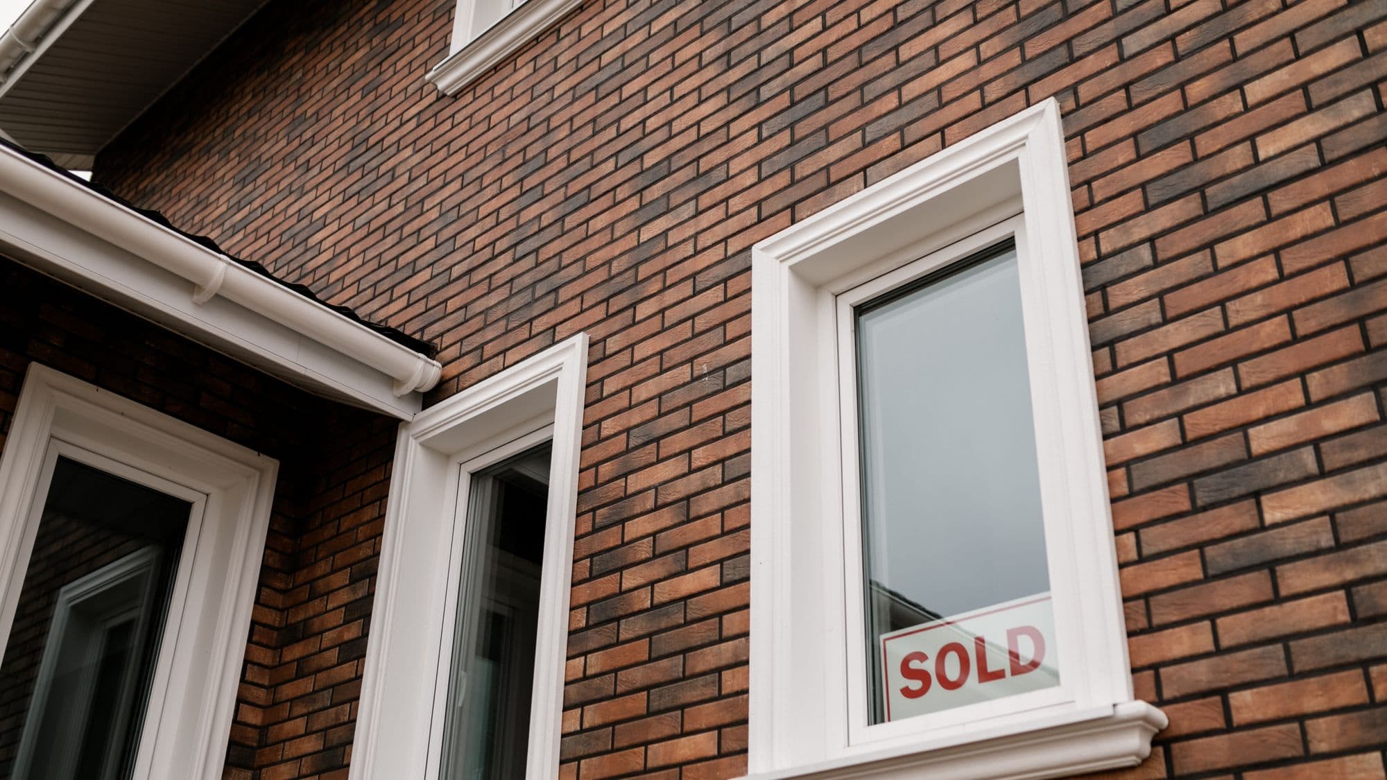 A sold sign in the window of a brick house