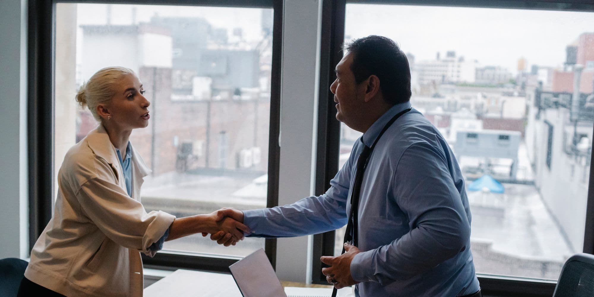 Two people shaking hands across a desk at the end of an interview