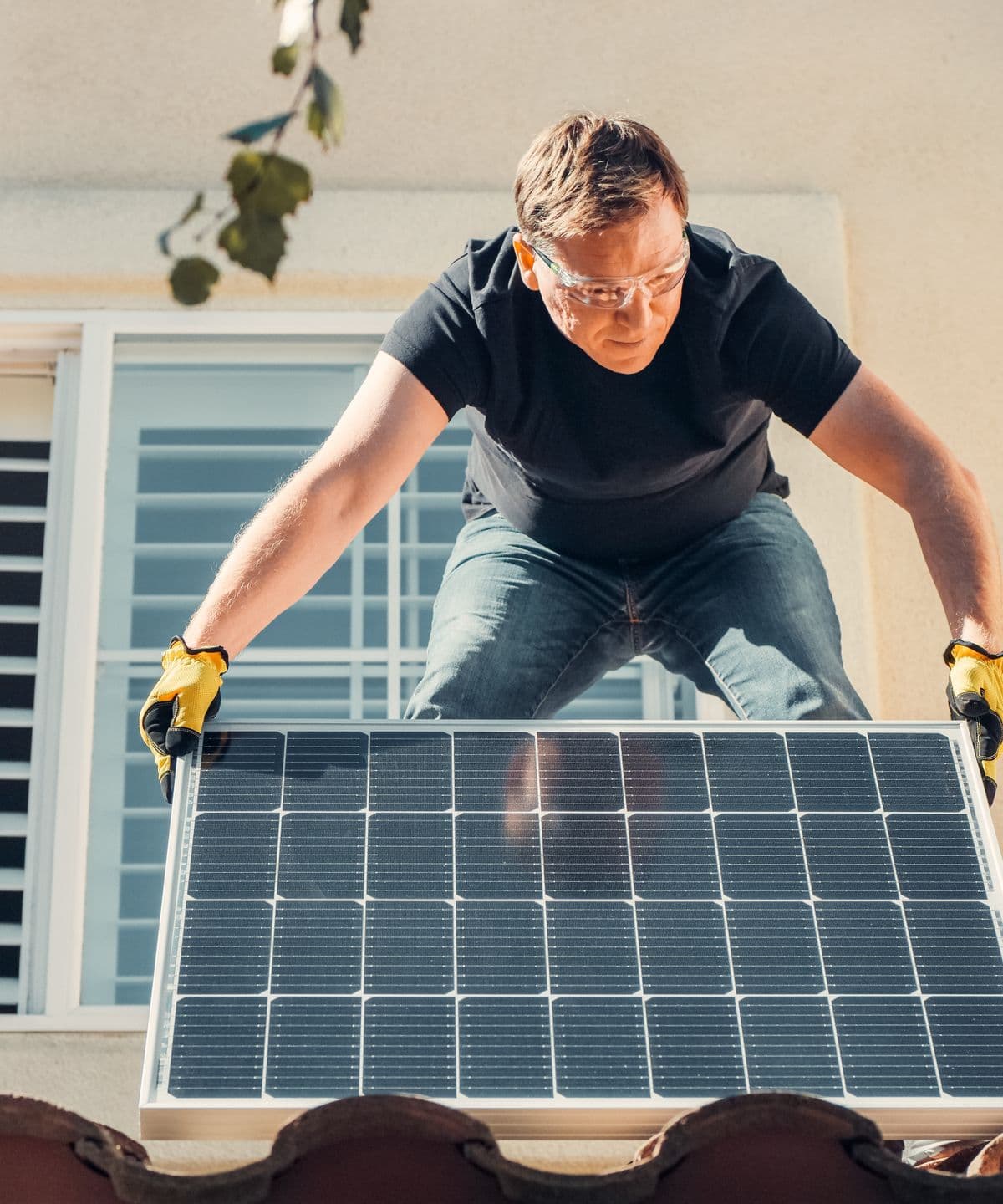 An installer in safety glasses lowering a solar panel into place on a roof
