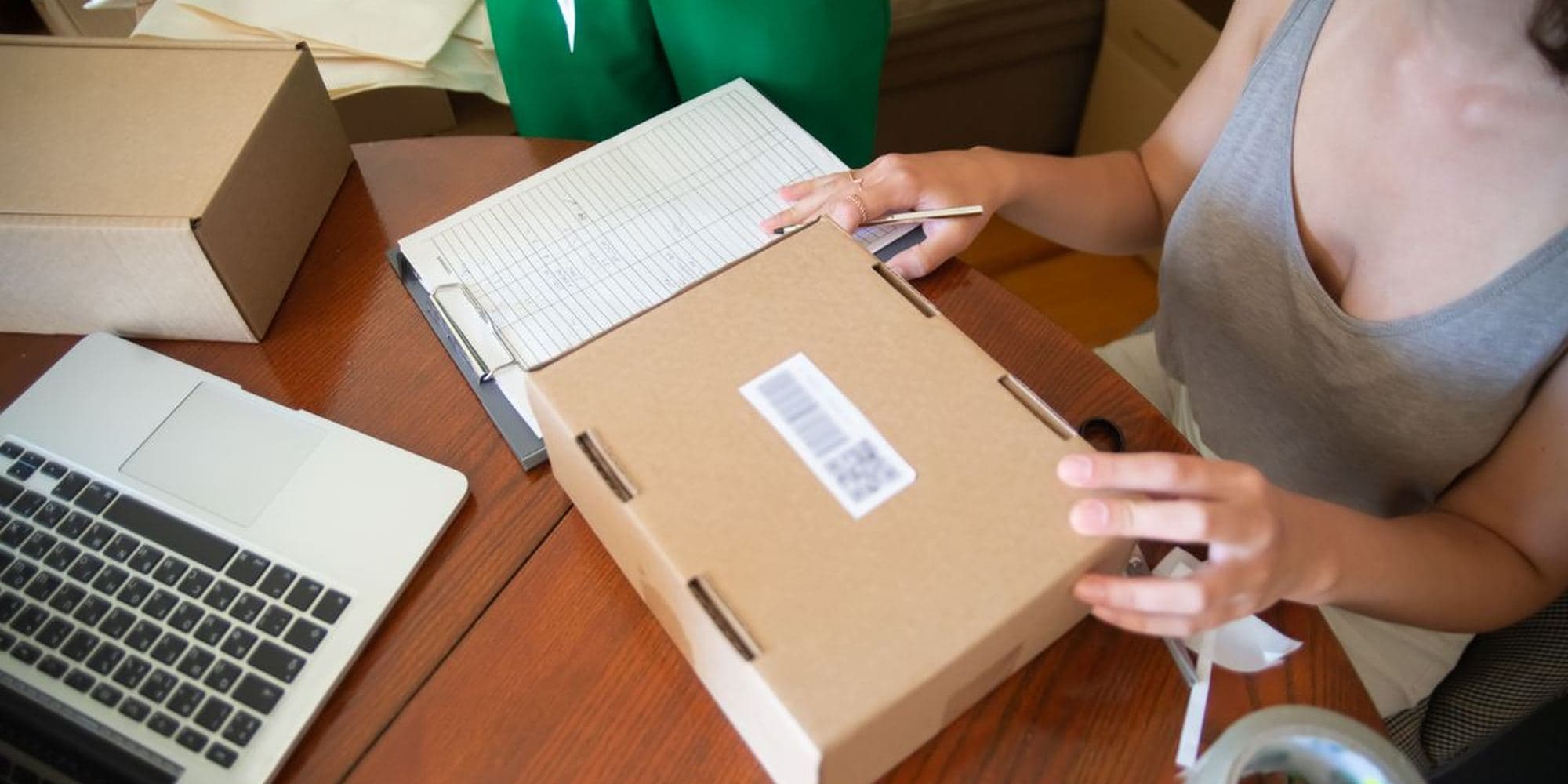 Someone packing a parcel at a desk beside a laptop