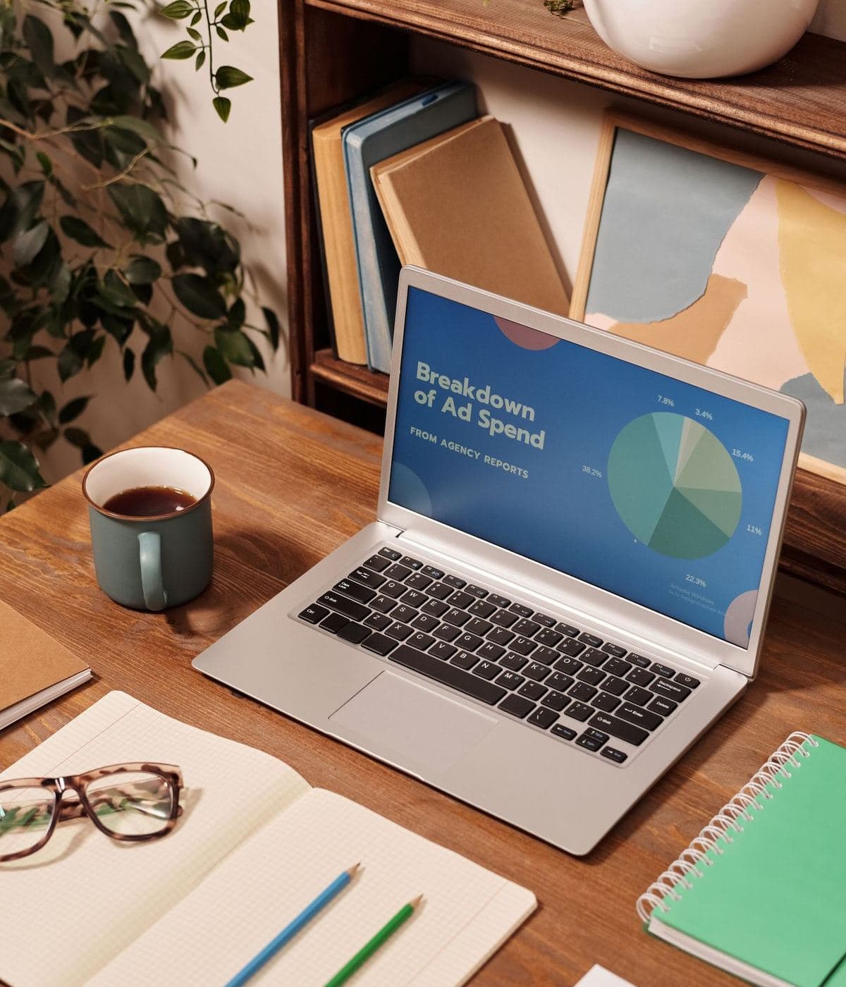 A laptop on a wooden desk showing a breakdown of ad spend, beside a cup of coffee